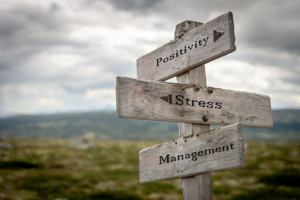 Workplace Stress: The Science Behind Prevention and Early Intervention Workplace stress, positivity, and management concepts shown on a wooden road sign, reflecting leadership training and corporate stress management by Ginny Estupinian, PhD