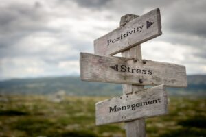 Workplace stress, positivity, and management concepts shown on a wooden road sign, reflecting leadership training and corporate stress management by Ginny Estupinian, PhD